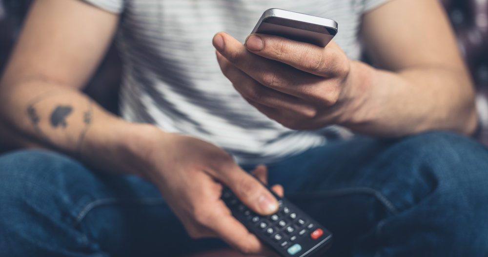 Person holding a phone and a TV remote